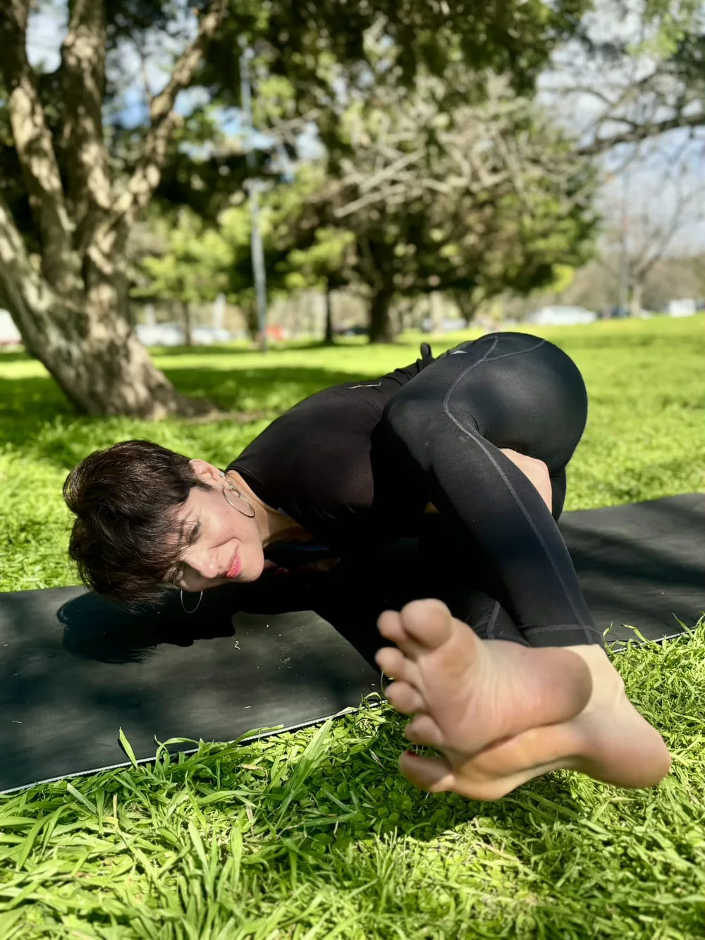 Flor Buale sobre el mat al aire libre, con una pierna por detrás del hombro